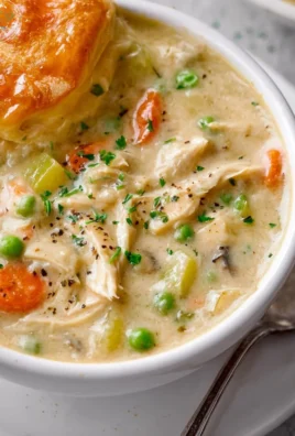 Delicious Chicken Pot Pie Soup in a bowl, topped with herbs and flaky pastry crust.