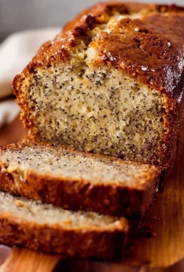 Loaf of moist banana bread on a wooden cutting board with bananas