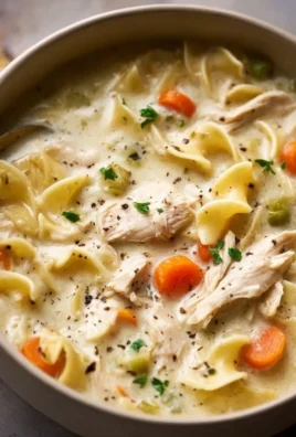 Bowl of creamy chicken noodle soup with vegetables and herbs